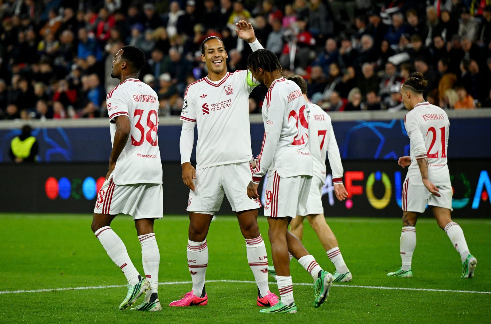 Virgil van Dijk, wearing the captain's armband, smiles and celebrates with Bradley Barcola as Ryan Gravenberch and Kostas Tsimikas walk past